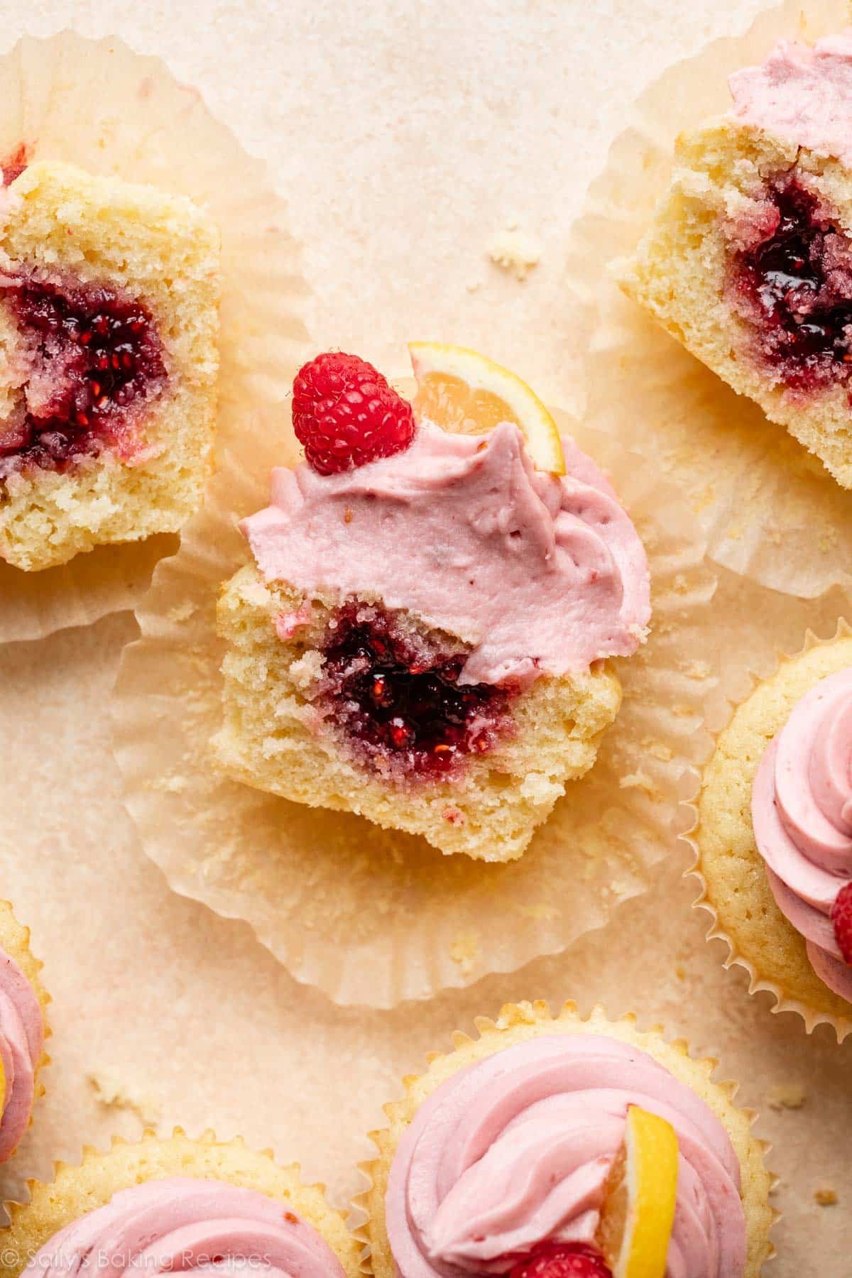 overhead photo of lemon raspberry jam cupcakes with a few cut in half to show the jam center.