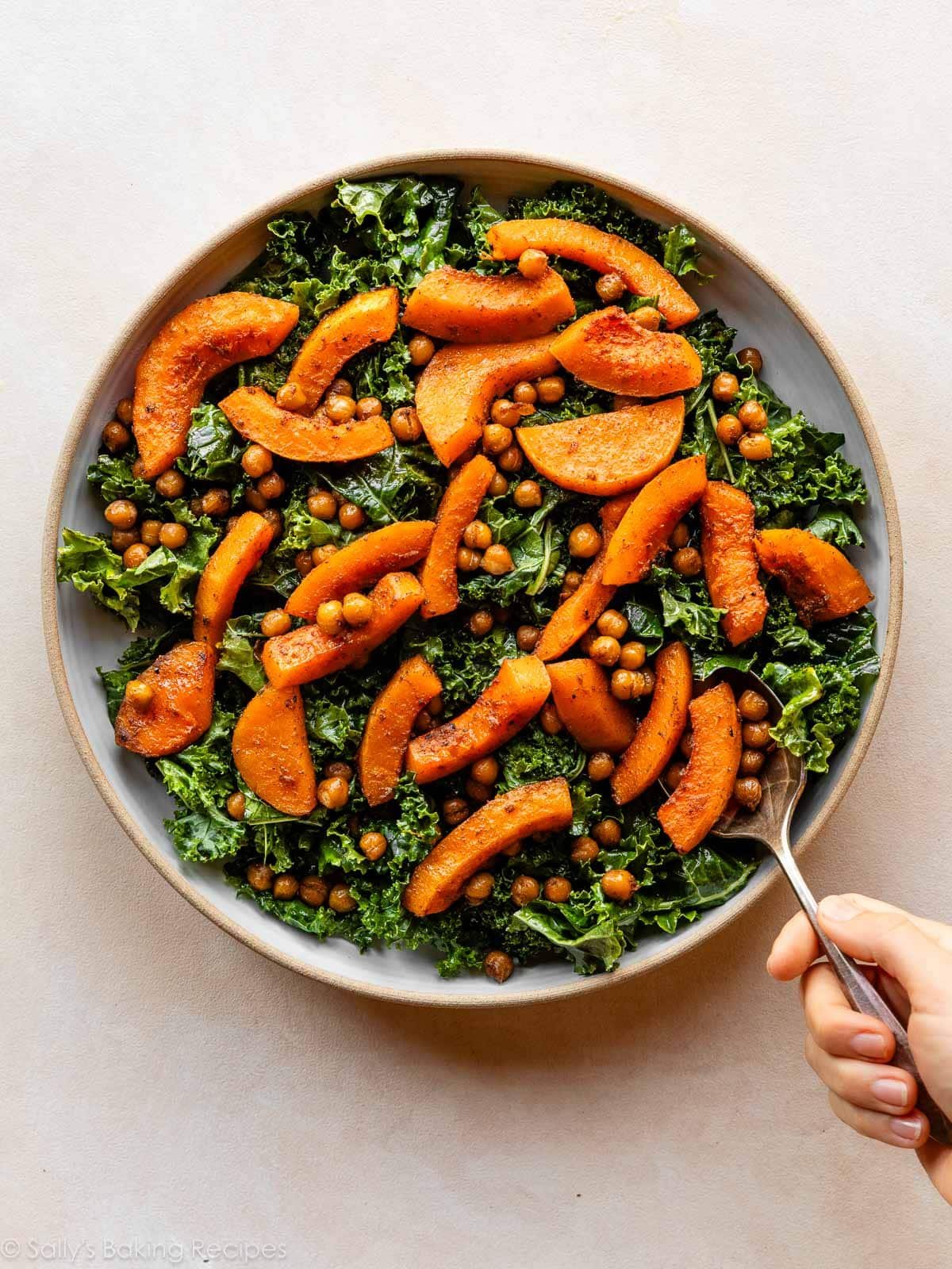 roasted sliced squash being spooned on top of kale.