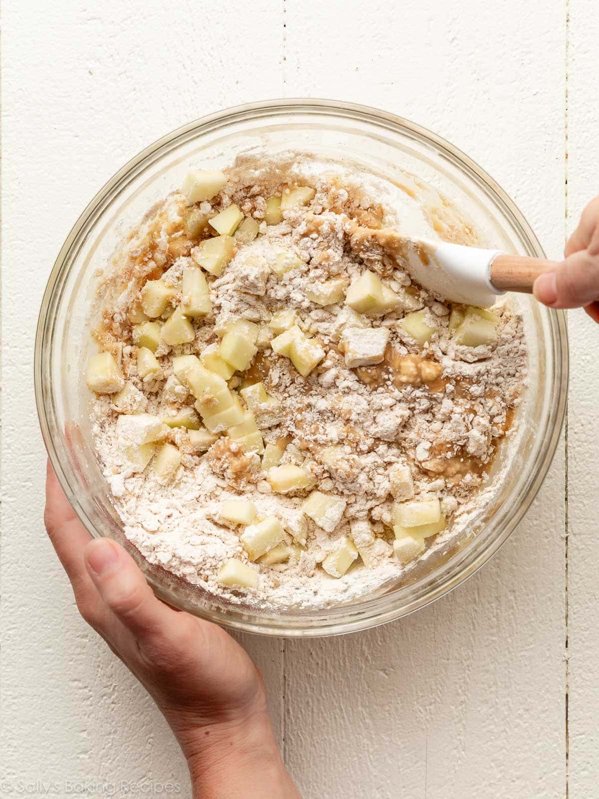 hands mixing dough with apples in it.