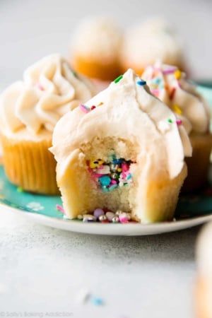 piñata cupcakes on a plate with a bite taken from one showing the sprinkles in the middle