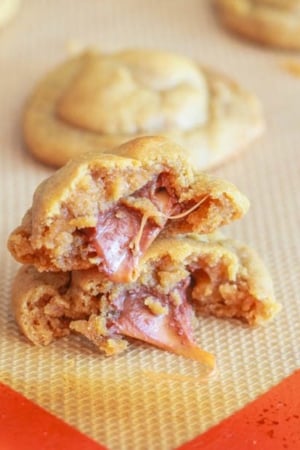 stack of peanut butter cookies stuffed with a Rolo on a silpat baking mat broken in half showing the inside