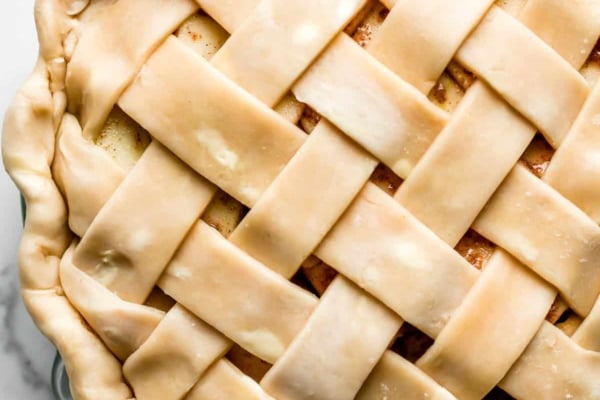 pie crust in lattice design on top of apple pie sitting in glass pie dish.