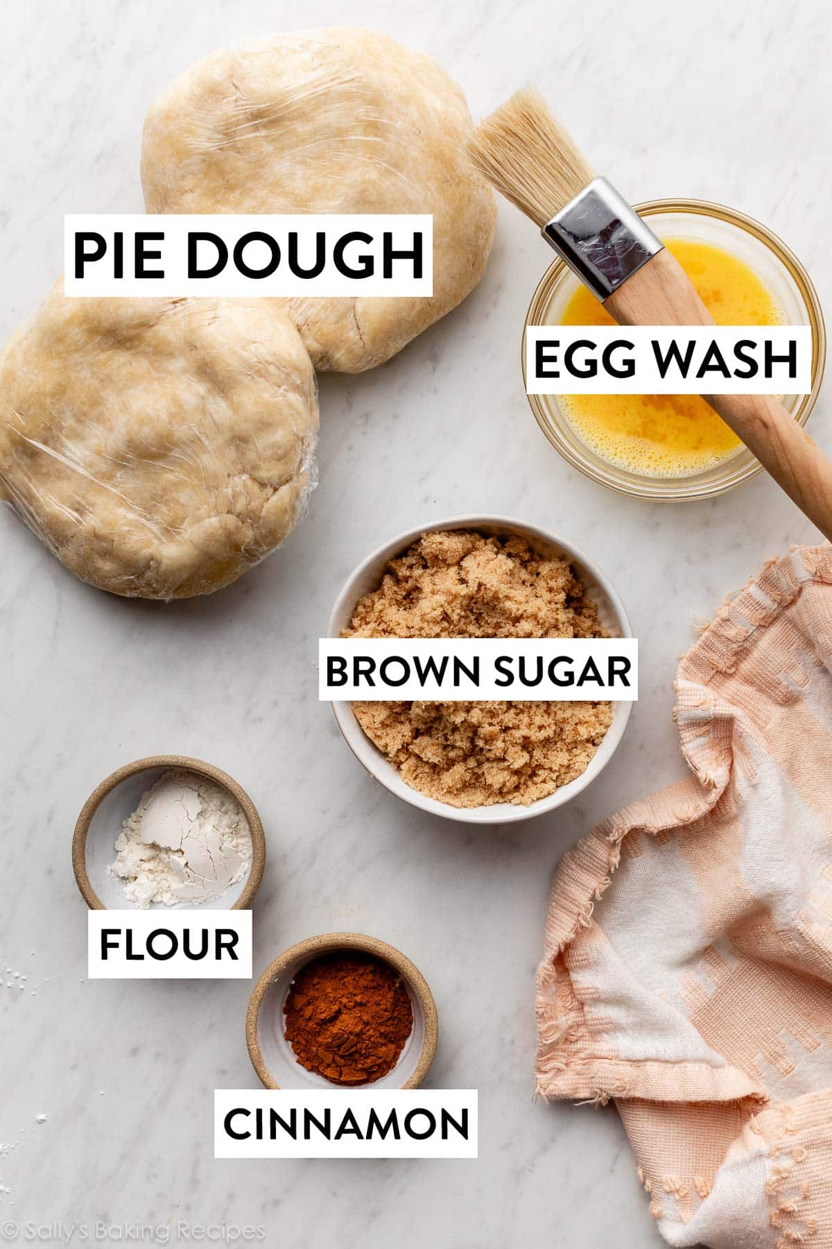 ingredients on marble counter including egg wash and pastry brush, flour, and pie dough.