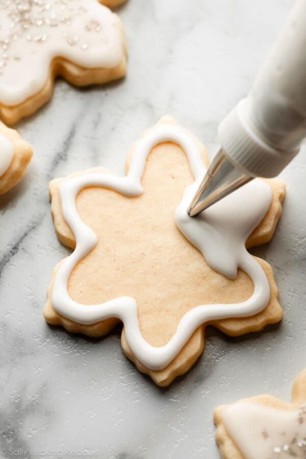 piping white icing on snowflake-shaped cookie.