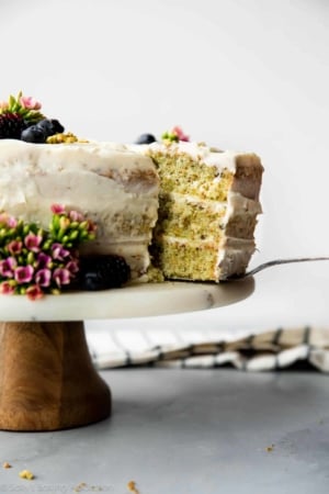 pistachio cake on a wood and marble cake stand with a slice on a cake server