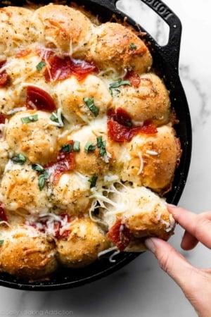 pulling a cheese pepperoni pizza roll out of cast iron skillet.