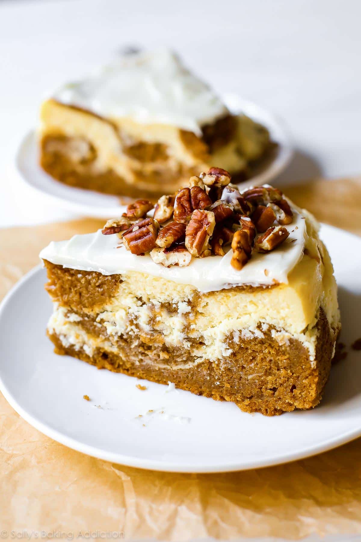 slice of pumpkin cake cheesecake with cream cheese frosting on a white plate