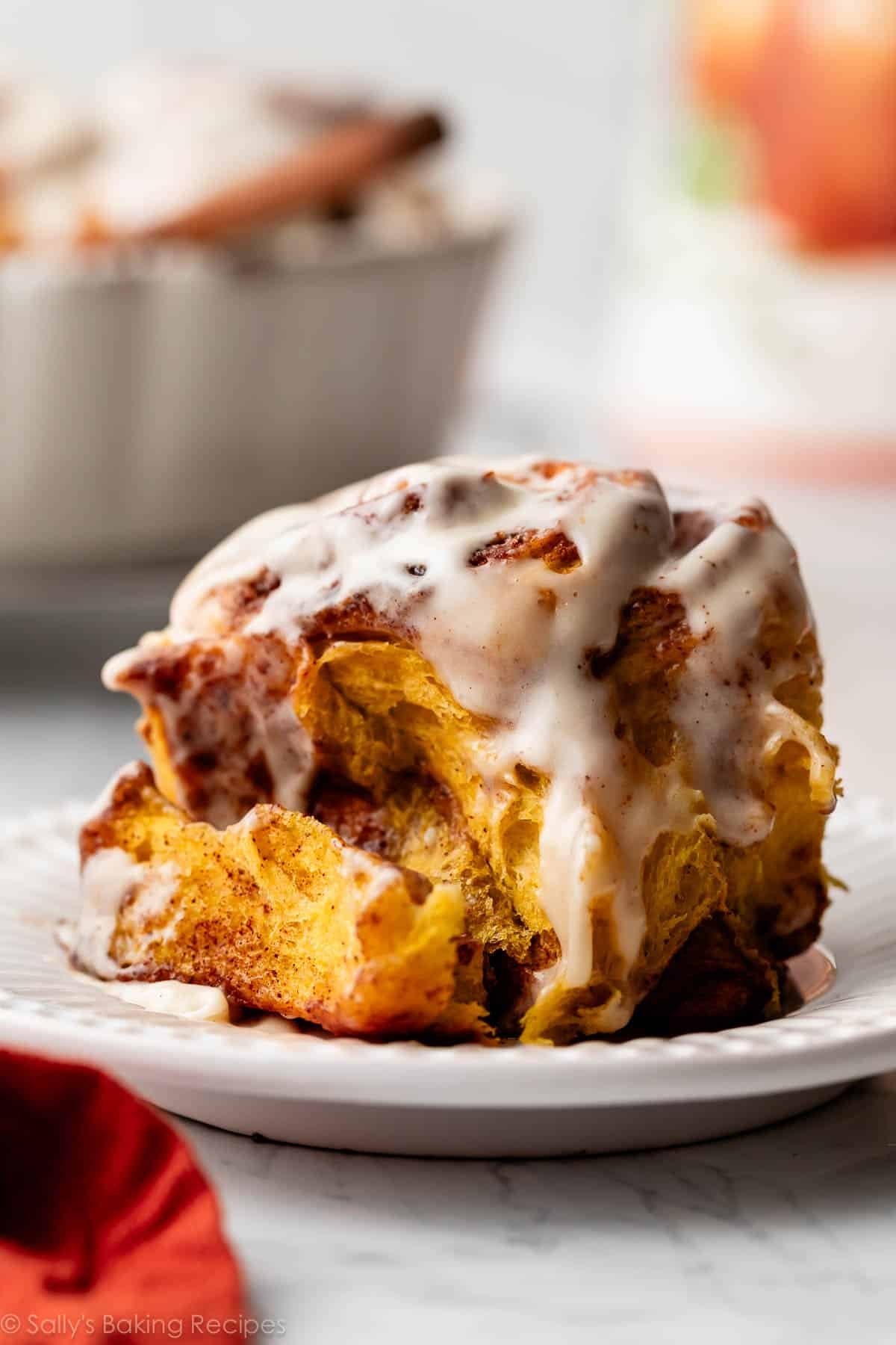 pumpkin cinnamon roll with maple icing on white plate.