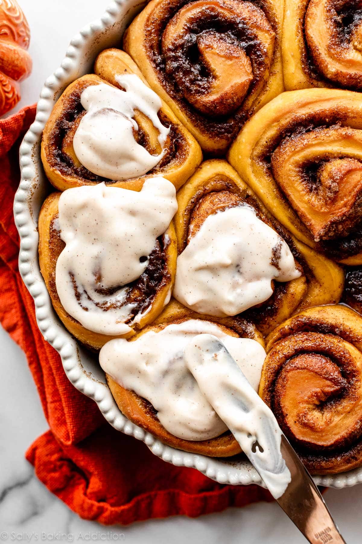 spreading icing on warm pumpkin cinnamon rolls