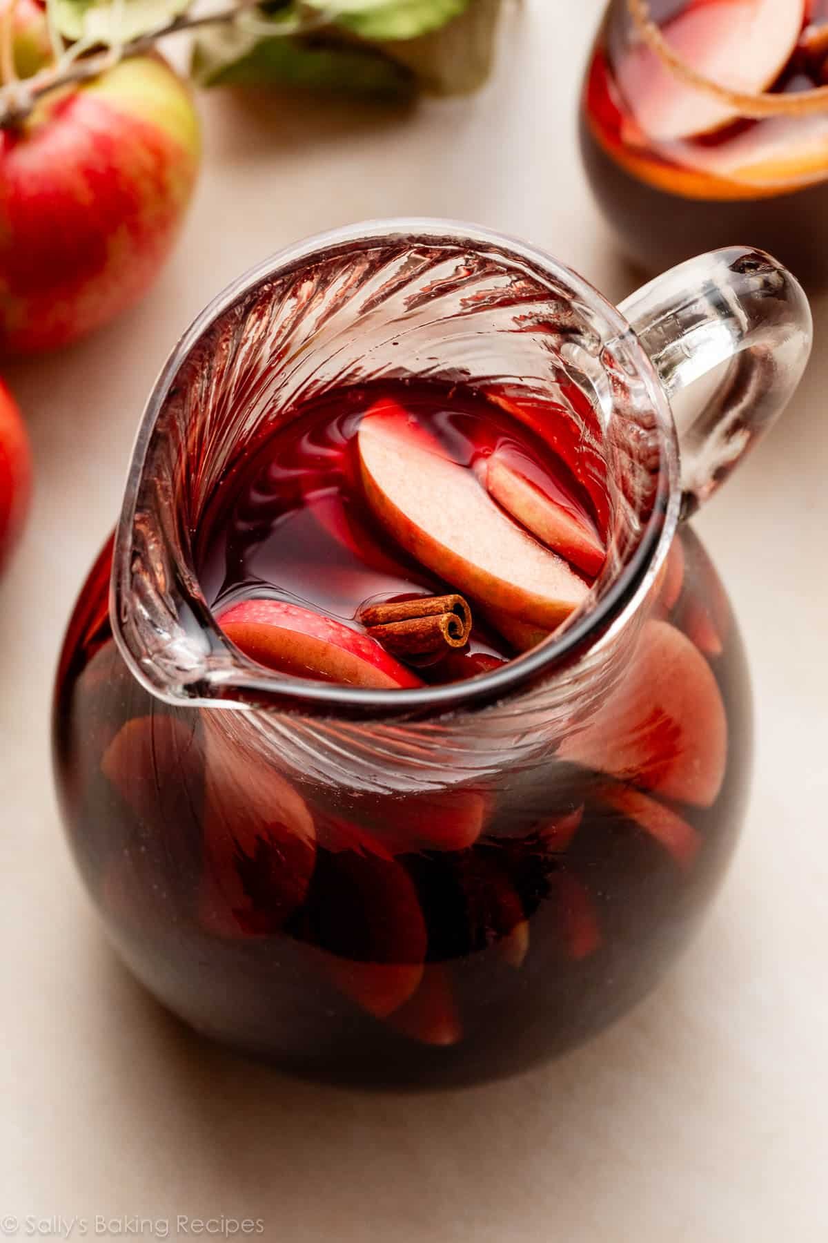 red apple sangria in pitcher with oranges, apples, and cinnamon stick.