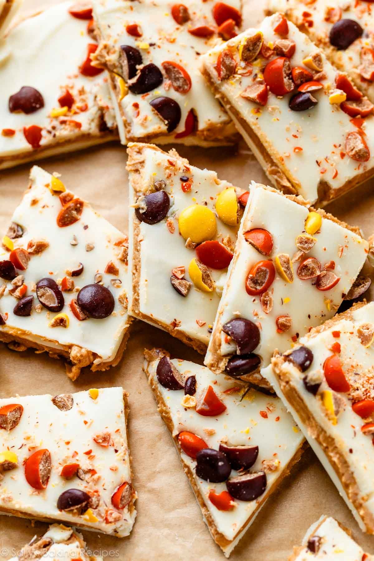 Reese's Pieces white chocolate peanut butter bark cut into pieces on brown parchment paper.