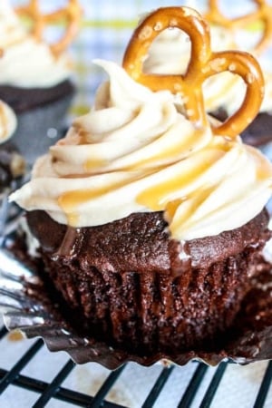 chocolate cupcakes topped with salted caramel frosting and a pretzel on a cooling rack