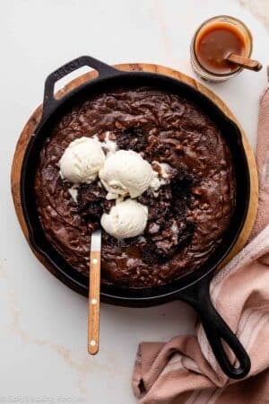 skillet brownie in cast iron skillet with vanilla ice cream and caramel sauce.