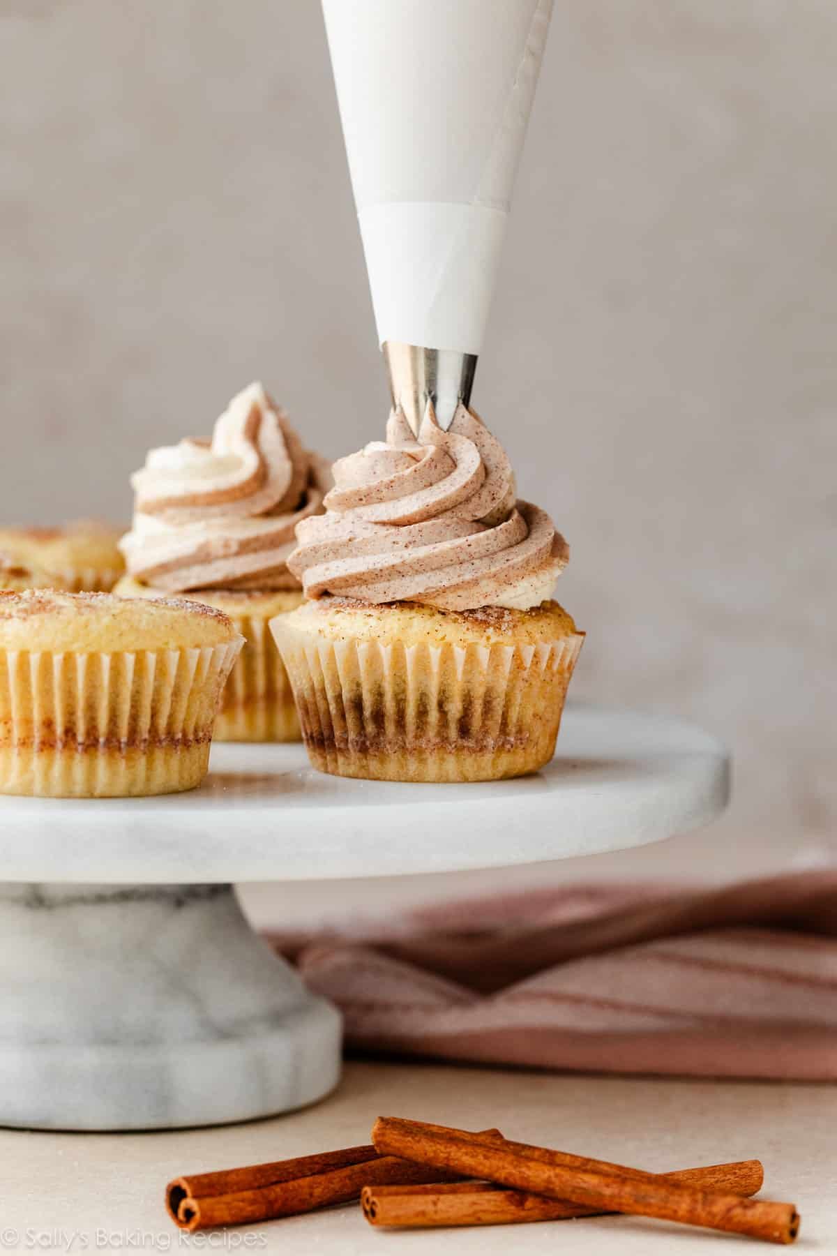 piping cinnamon frosting on top of a cinnamon swirl cupcake.