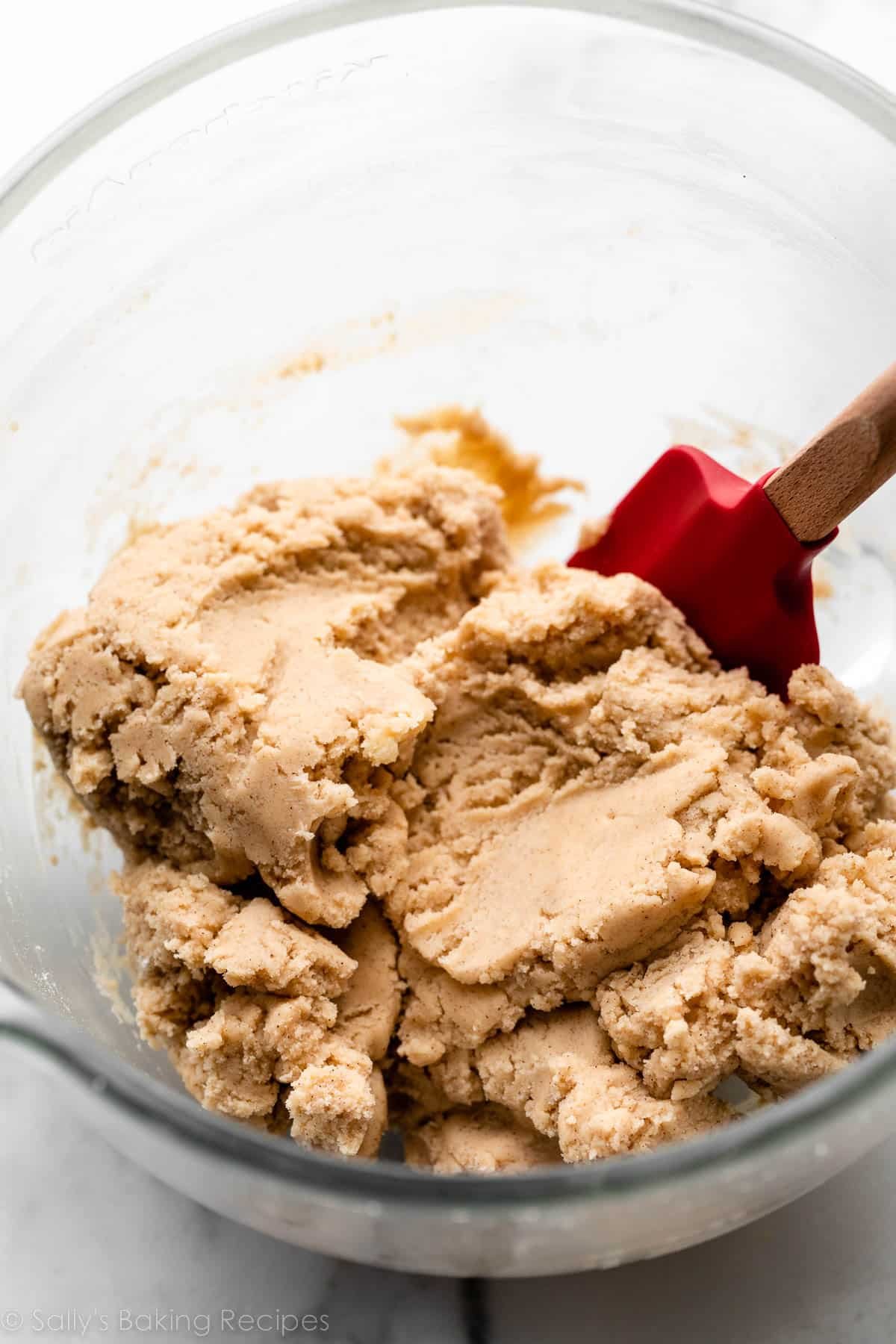 snickerdoodles cookie dough with red spatula in glass bowl.