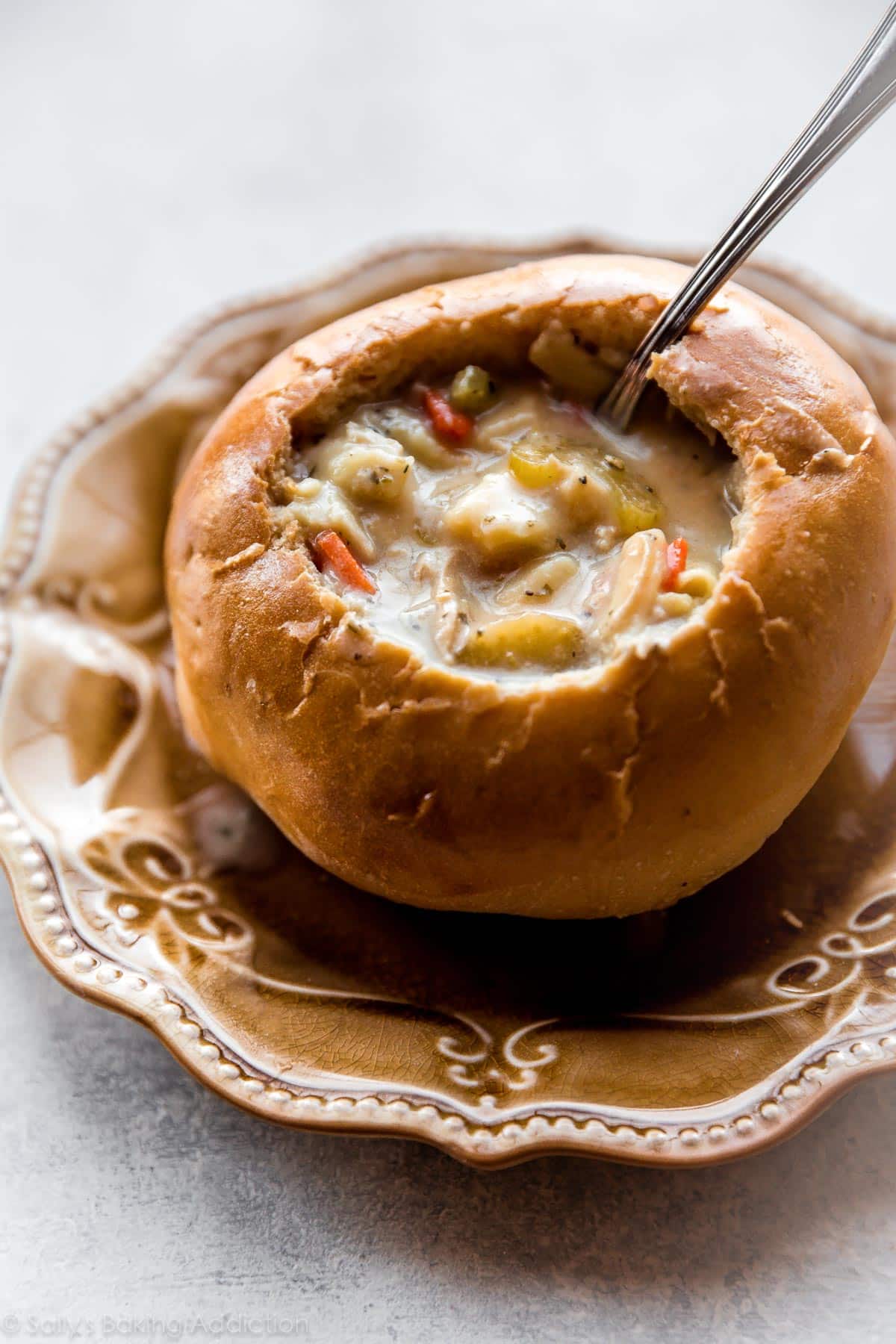 Chicken noodle soup in a bread bowl on a tan plate