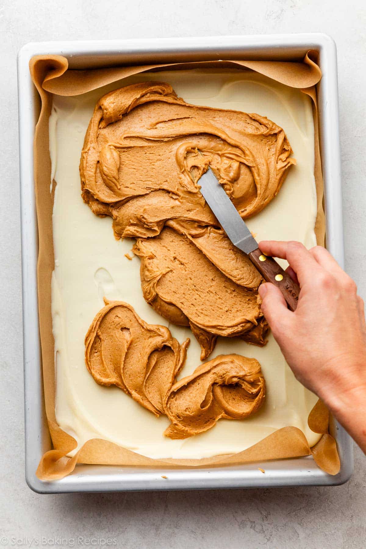 hand spreading peanut butter on top of chocolate set in pan.