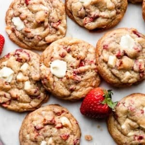 white chocolate strawberries & cream cookies on marble backdrop with fresh strawberry and white chocolate chunks.