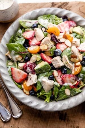 salad in gray dish including chicken, strawberries, mandarin oranges, blueberries, spinach, and avocado with poppy seed dressing on top.