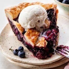 slice of triple berry pie with vanilla ice cream melting on top.