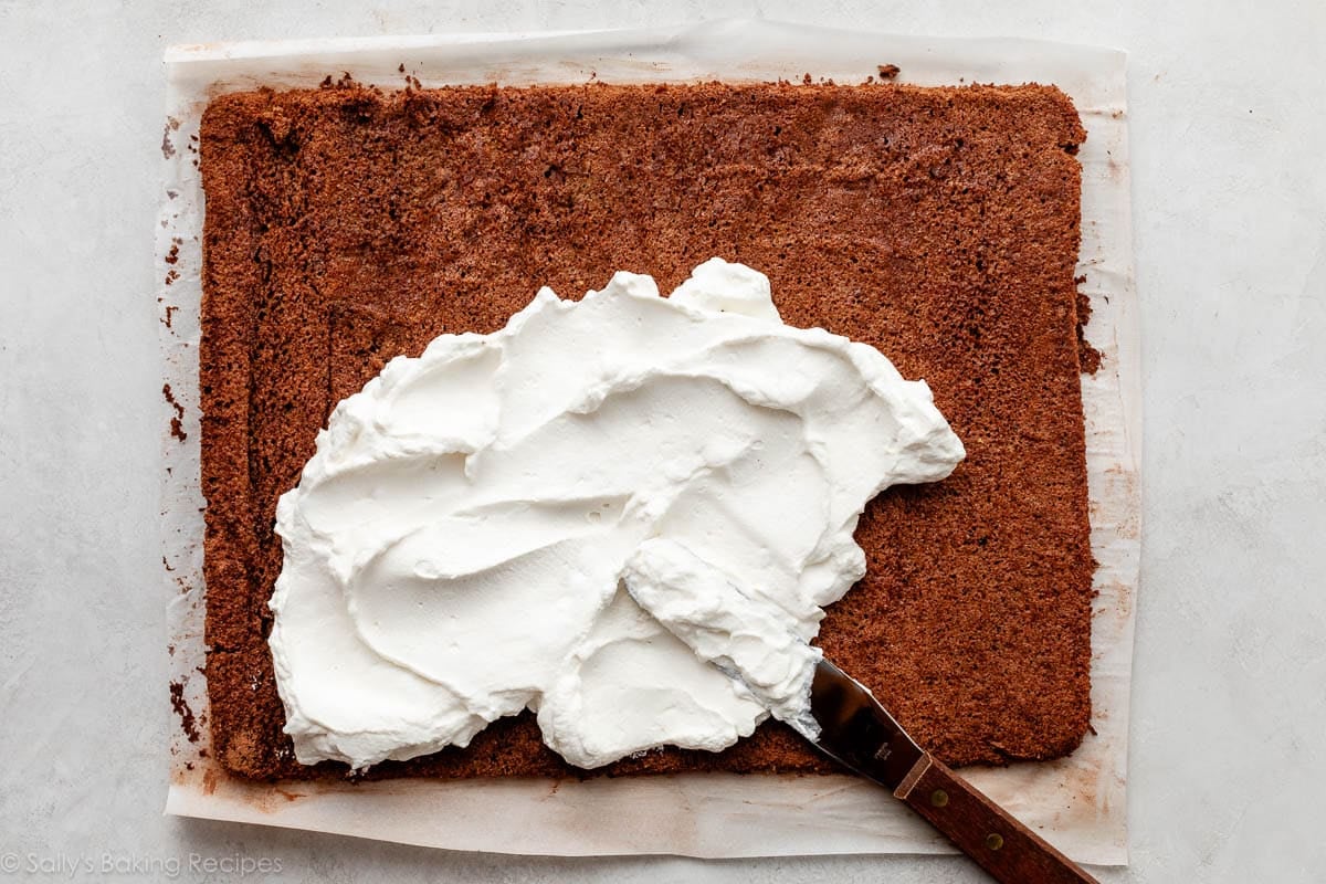 whipped filling being spread on large flat cake.