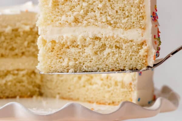 slice of white cake being taken away from cake stand.