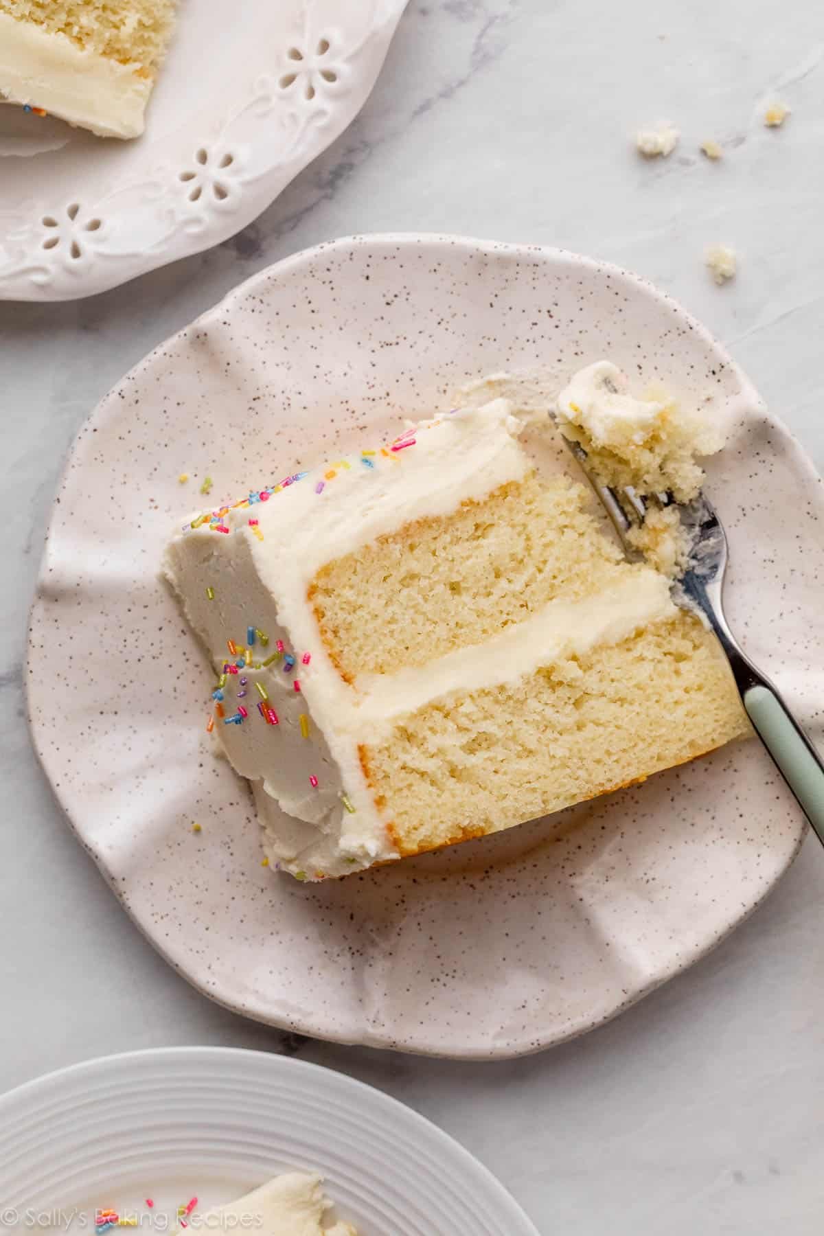 slice of white cake with forkful taken out on ruffled ceramic plate.