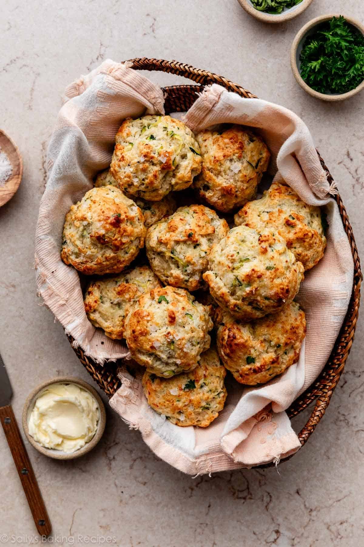 zucchini biscuits in pink linen-lined basket with butter and fresh herbs.